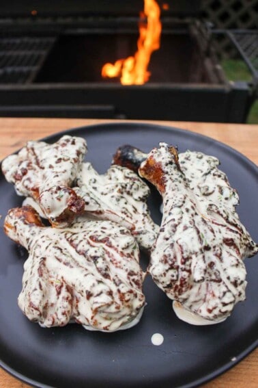 Butterflied Chicken Drumsticks with Jalapeño Lime White Sauce sitting on a serving plate in front of a fire.