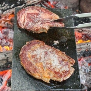 Steaks on a rock cooking with flames all around them.