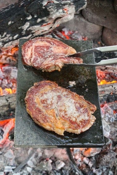 Steaks on a rock cooking with flames all around them.