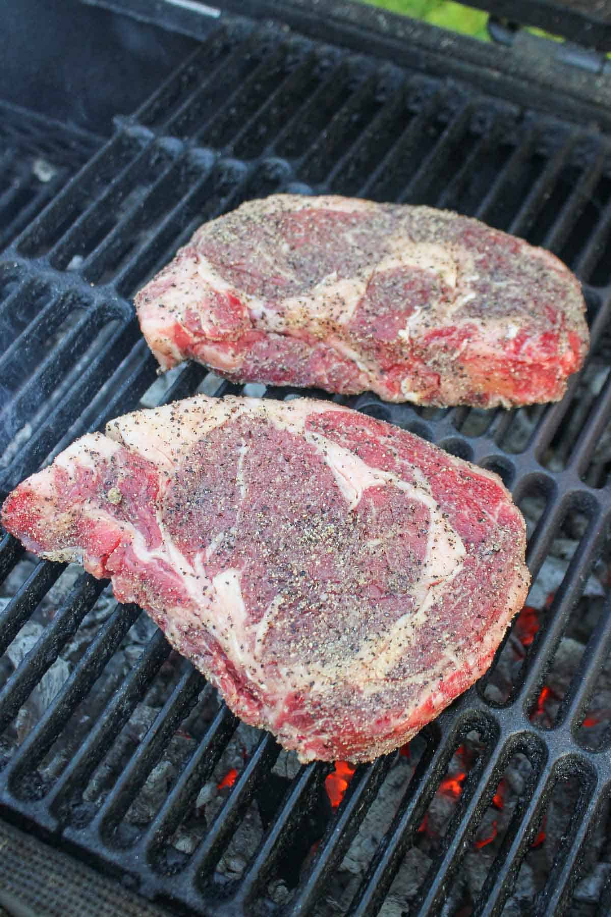 Adding the seasoned ribeyes to the grill so they can start cooking.
