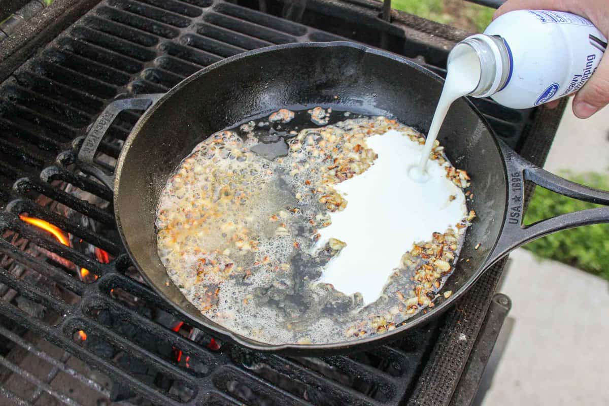 Adding heavy whipping cream to the cast iron skillet.