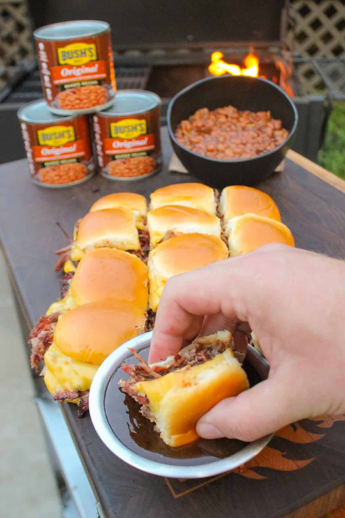 Dipping the slider in the au jus with the baked beans in the background.