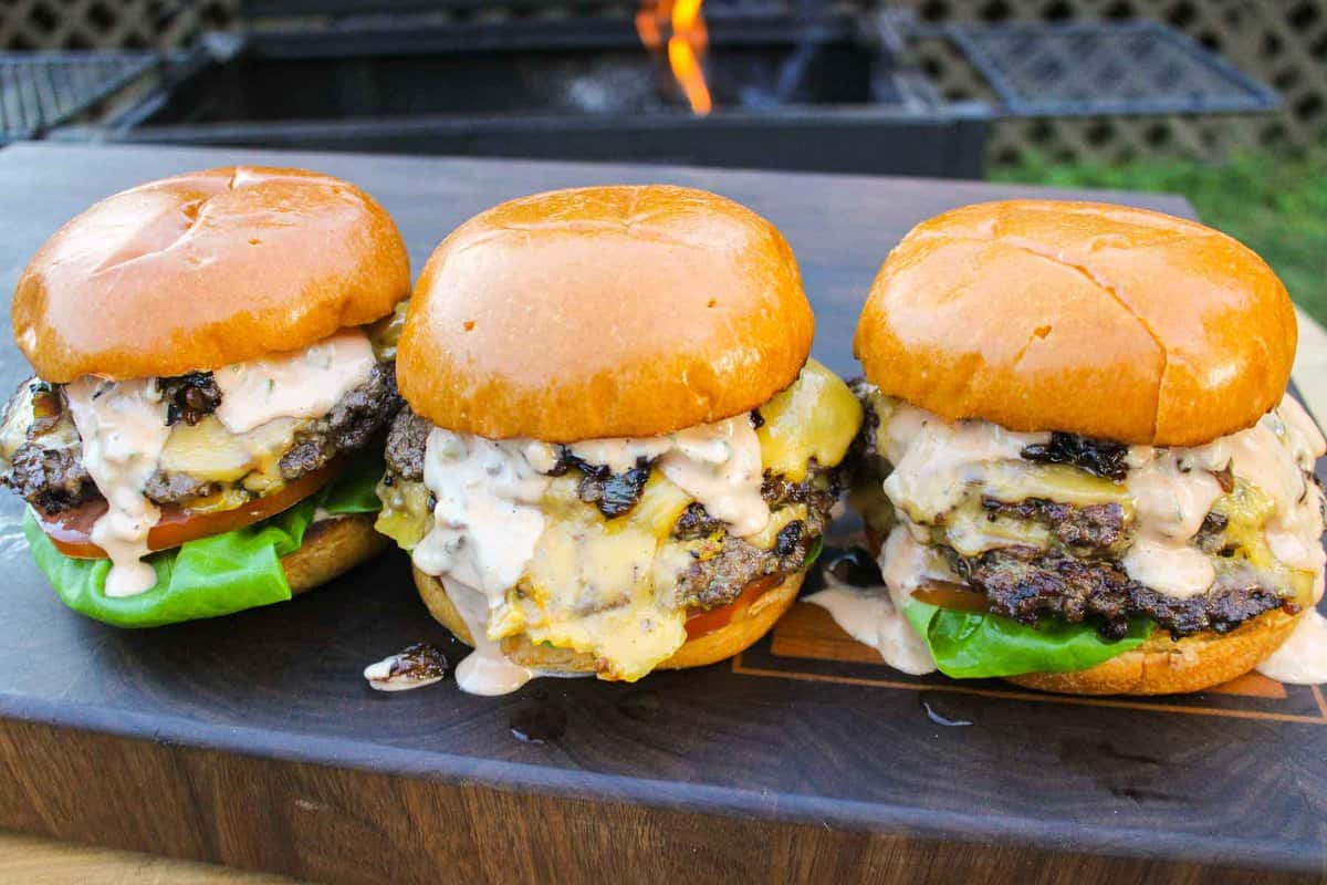 Three of the animal style burgers sitting on a cutting board together.