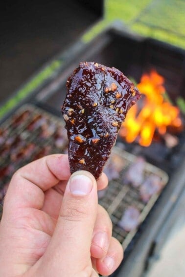 A piece of Hot Honey Garlic Beef Jerky held up close to the camera.