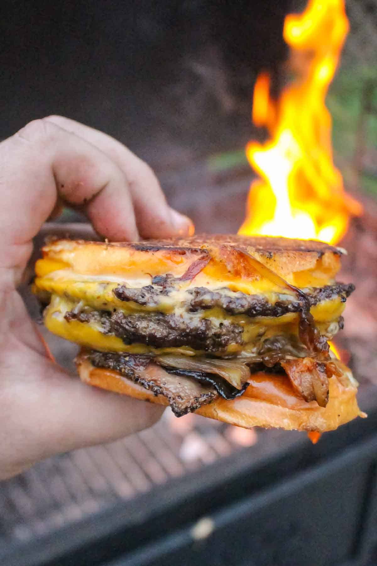 A close up shot of an animal style patty melt held next to the fire.