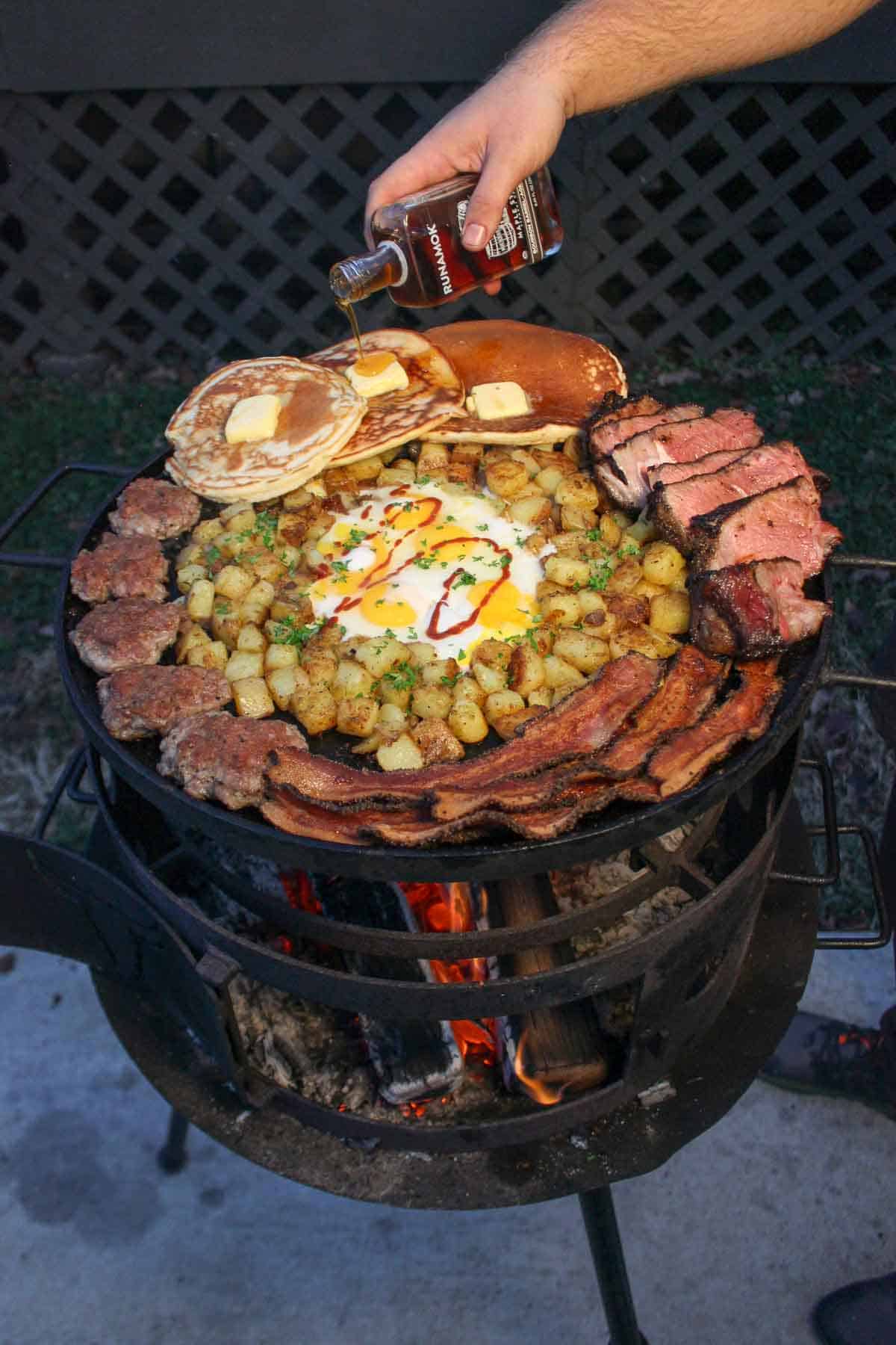 The ultimate Country Breakfast Skillet comes together on the grill with bacon, country sausage, crispy potatoes, fried eggs, pancakes, and sliced ribeye steak! 