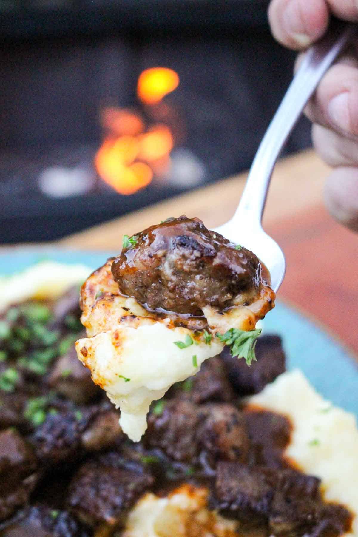 Steak and mashed potatoes and gravy is served up on a spoon. 