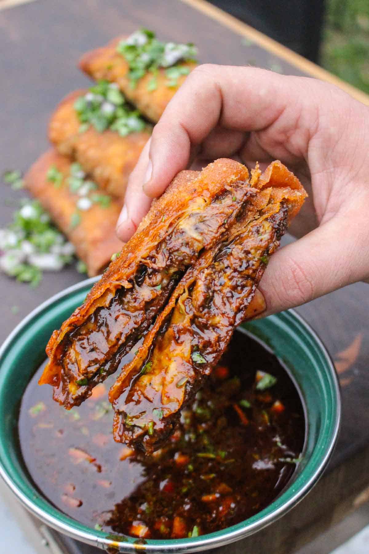 Birria Egg Rolls are dipped in the braising liquid for the perfect bite. 