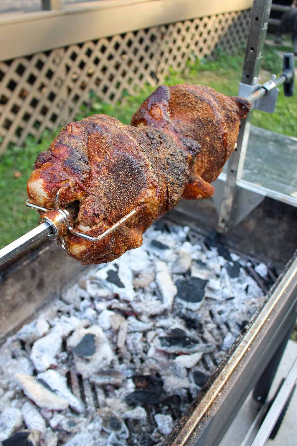 Two whole chickens on the rotisserie, cooking over the coals. 