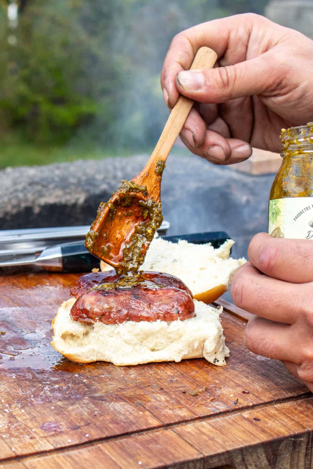 Adding chimichurri to a choripan.