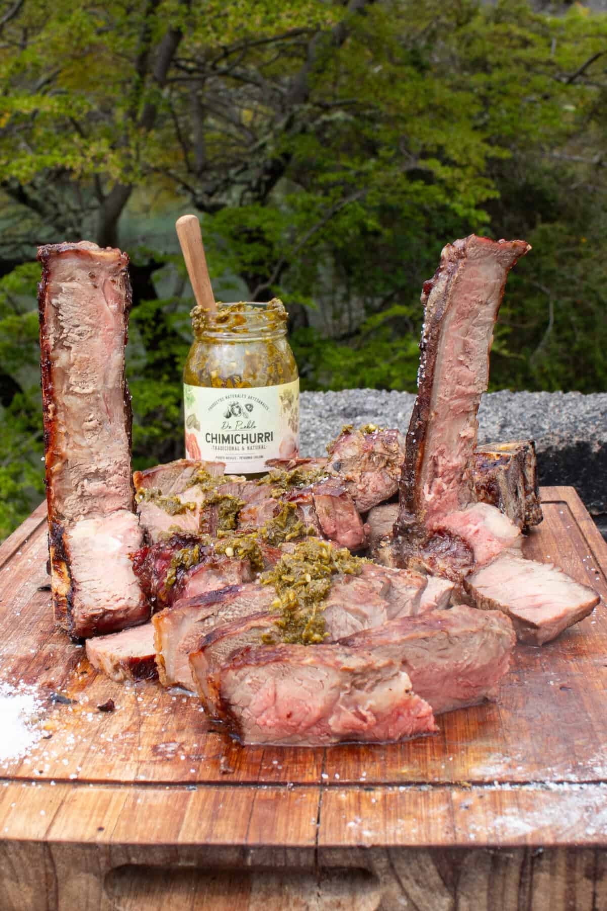 A cutting board full of sliced steak, topped with chimichurri. 