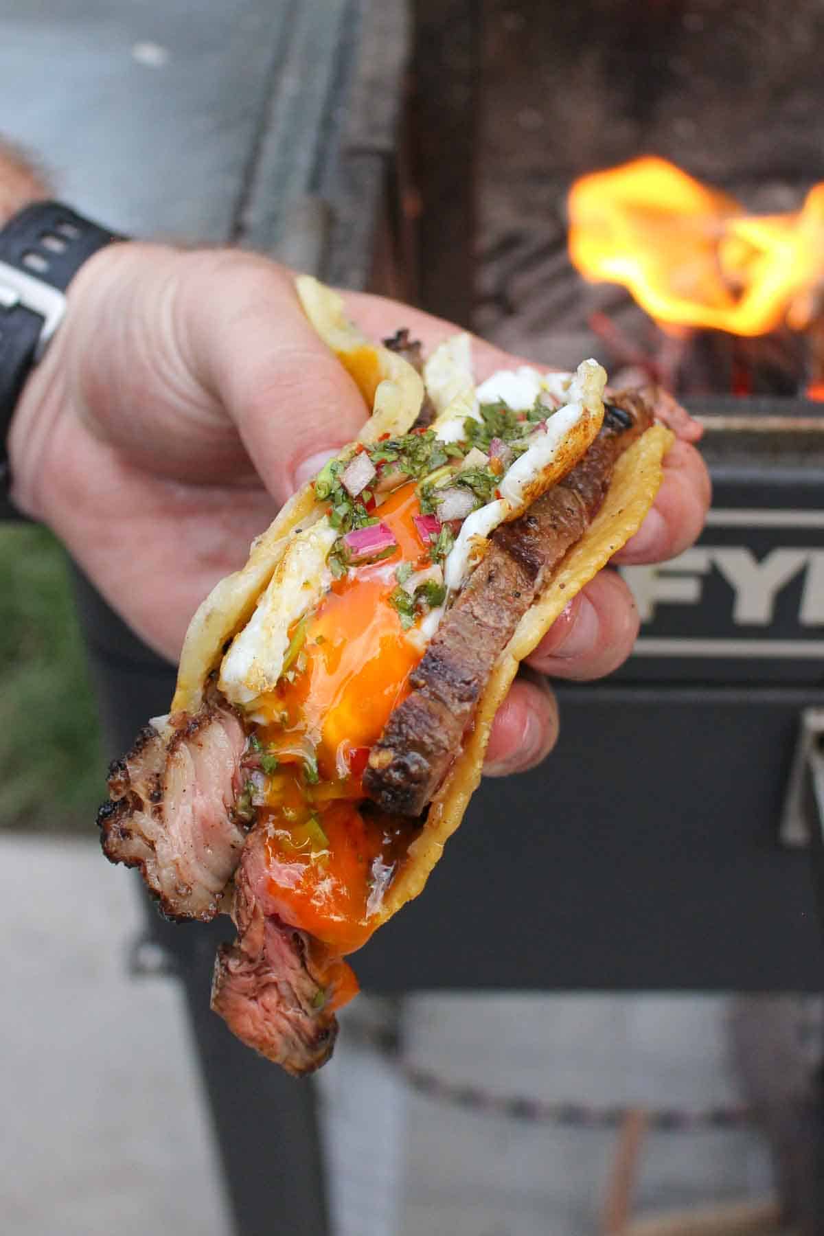 A steak and egg taco being held up to the camera so you can see the egg yolk running down the taco. 