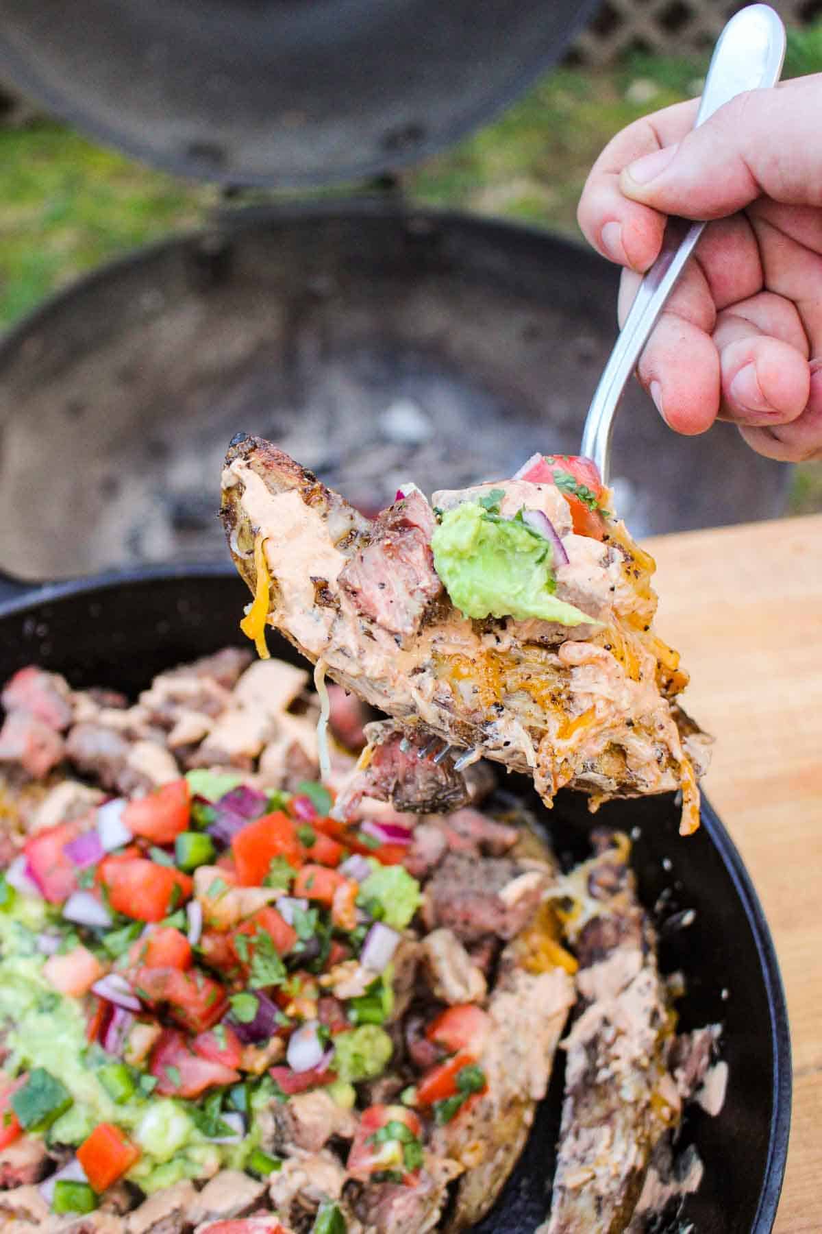 A potato wedge bite with cheese, steak and guacamole. 