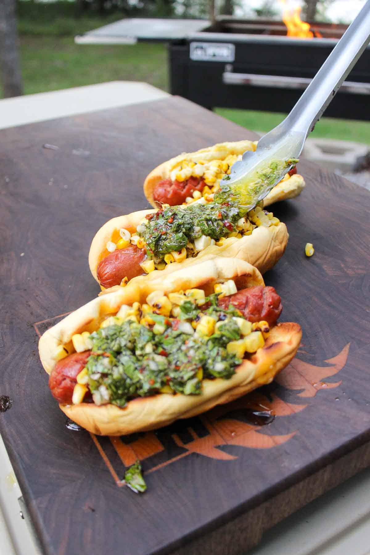 Grilled hot dogs topped with corn and chimichurri