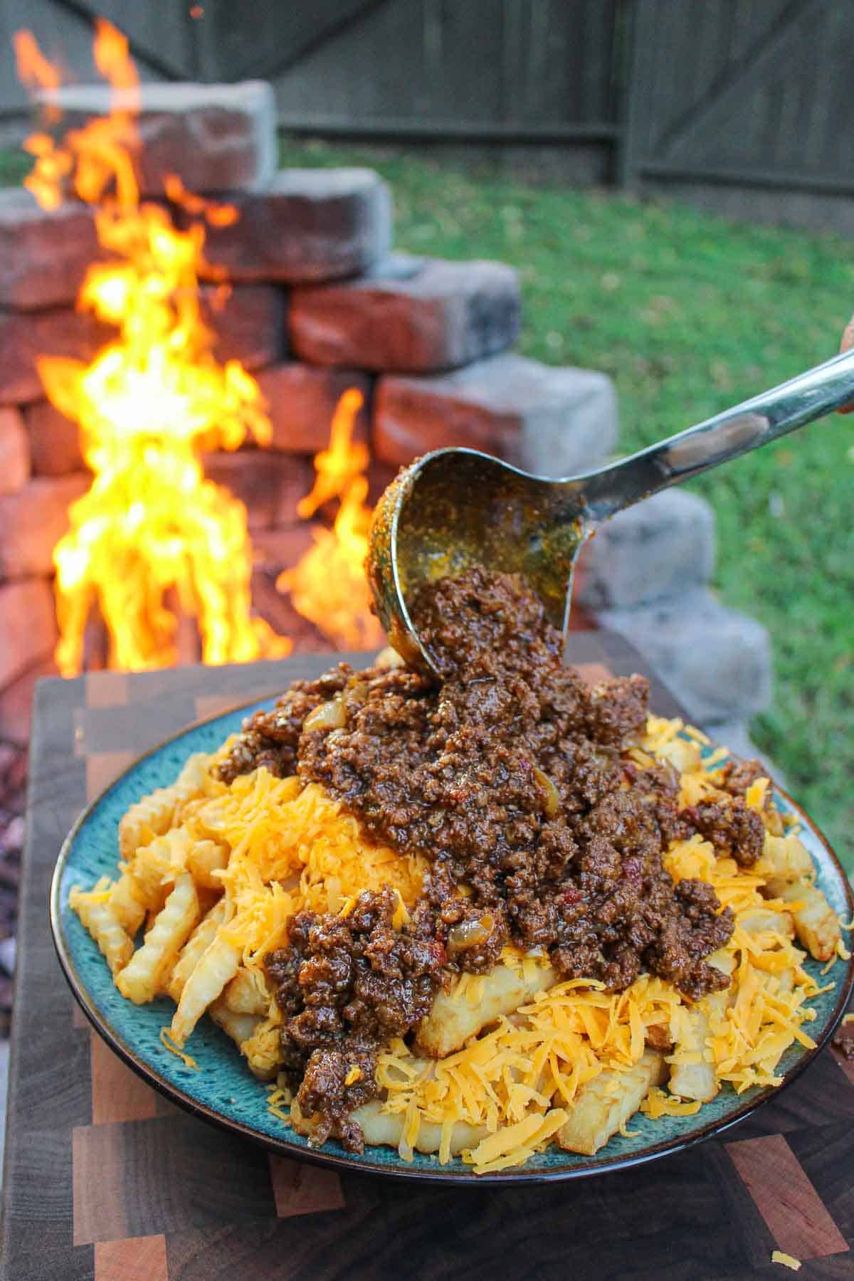 A ladle full of birria getting added on top of fries. 