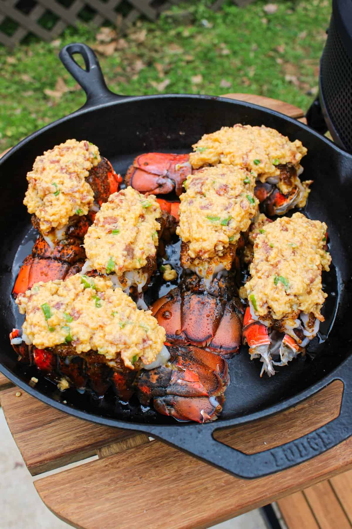 Bacon stuffed lobster tails in a cast iron skillet with breaded filling on  top for best lobster recipes