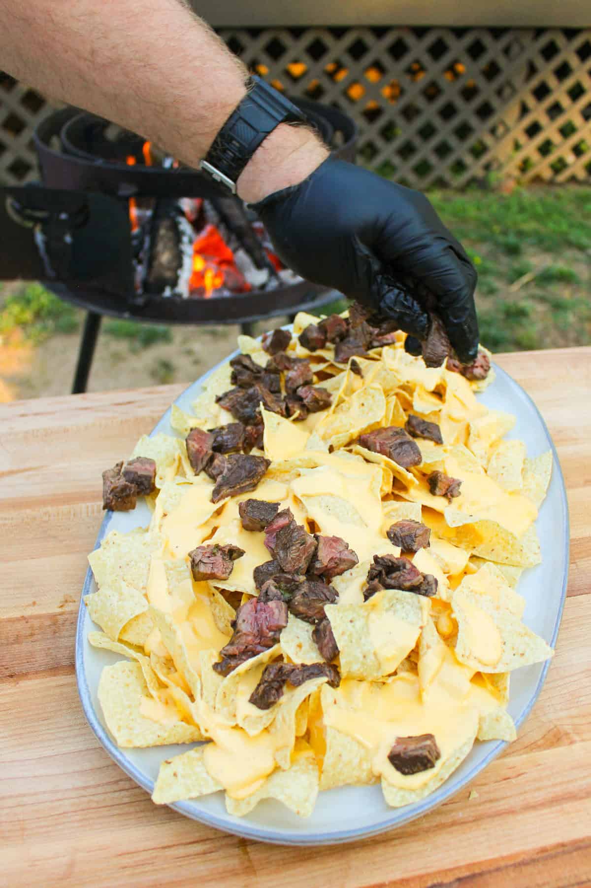 Adding chopped steak on top of some cheesy nacho chips.