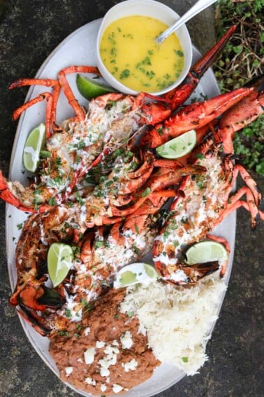 Coal roasted baja lime lobsters cut open on a platter with limes and melted butter for serving