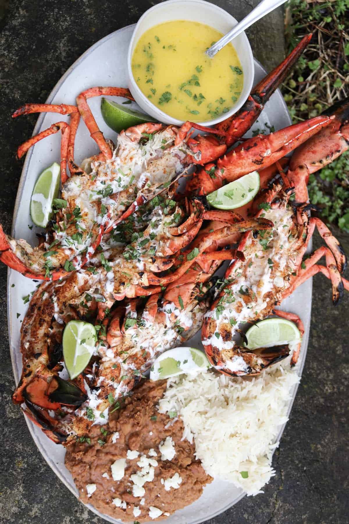 Coal roasted baja lime lobsters cut open on a platter with limes and melted butter for serving