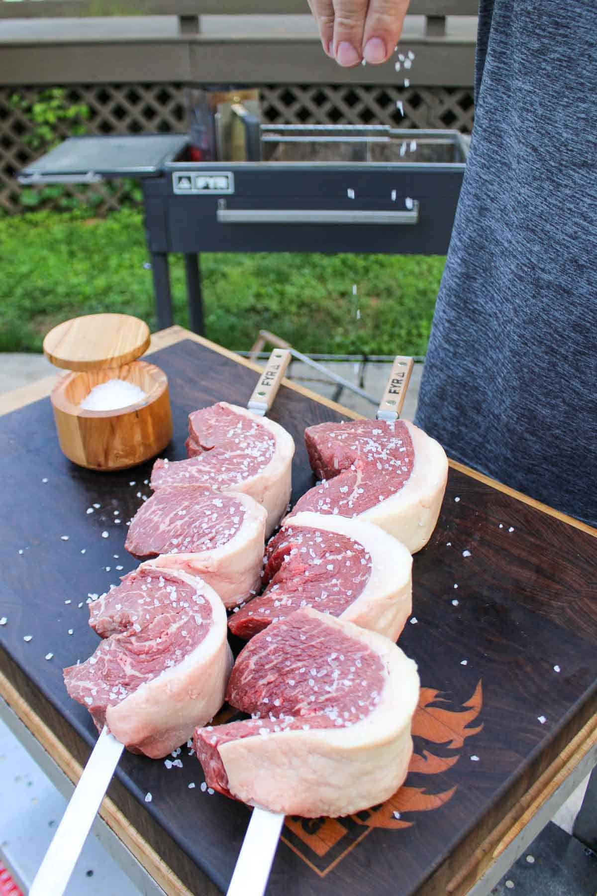 Seasoning the raw picanha on the skewers with course salt.