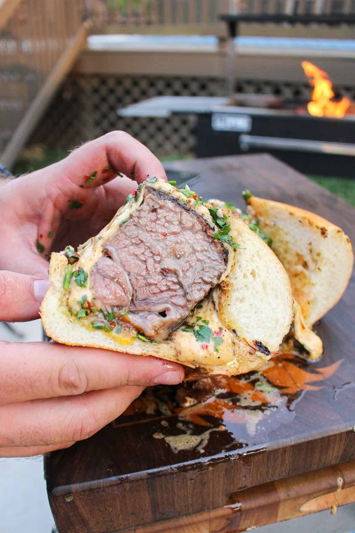 A beef rib sandwich cut in half and held up to the camera so you can see it's dripping juices.