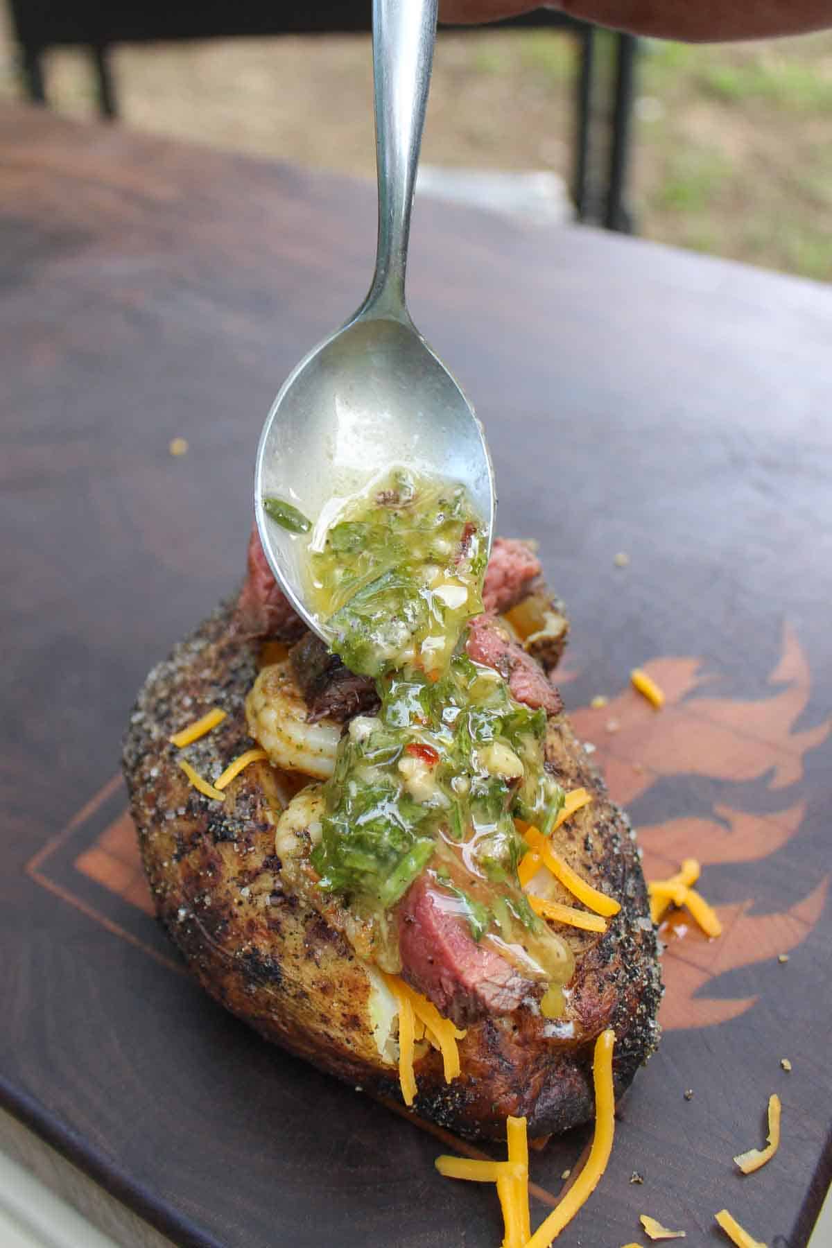 Spooning chimichurri butter over the surf and turf baked potato with all the fixings