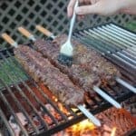 Using a brush to baste flake steak skewers on the grill with cowboy butter