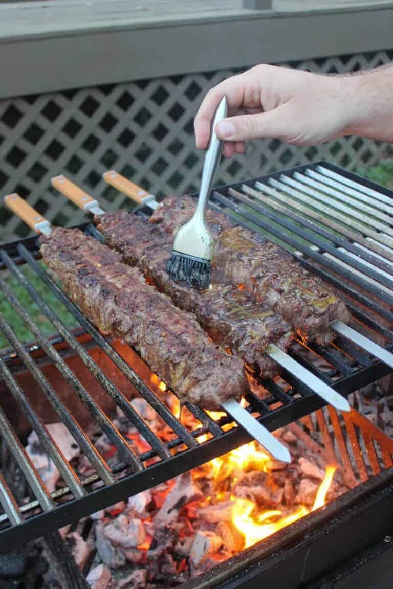 Using a brush to baste flake steak skewers on the grill with cowboy butter