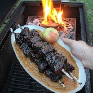 Smoked pork belly burnt ends with applesauce, held next to a grill fire with apples on the side