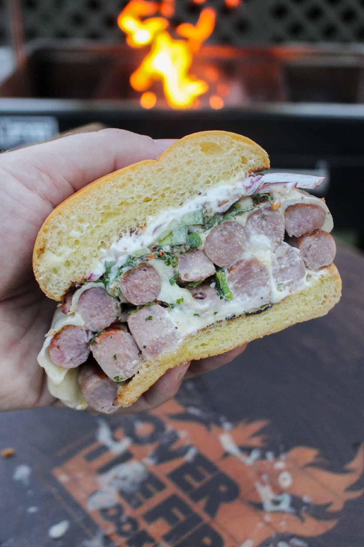 The Choripan Burger is sliced in half, showing all the delicious sausage that we perfectly cooked on the grill and paired with mozzarella and chimichurri.