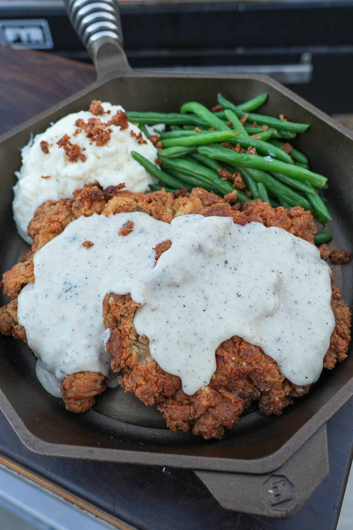 A close up of the fried steak smothered in the cream gravy, paired with mashed potatoes and green beans.