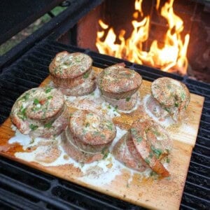 Finished smoked salmon pinwheels on a wood plank in front of a smoker