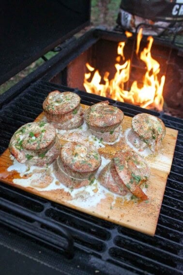 Finished smoked salmon pinwheels on a wood plank in front of a smoker