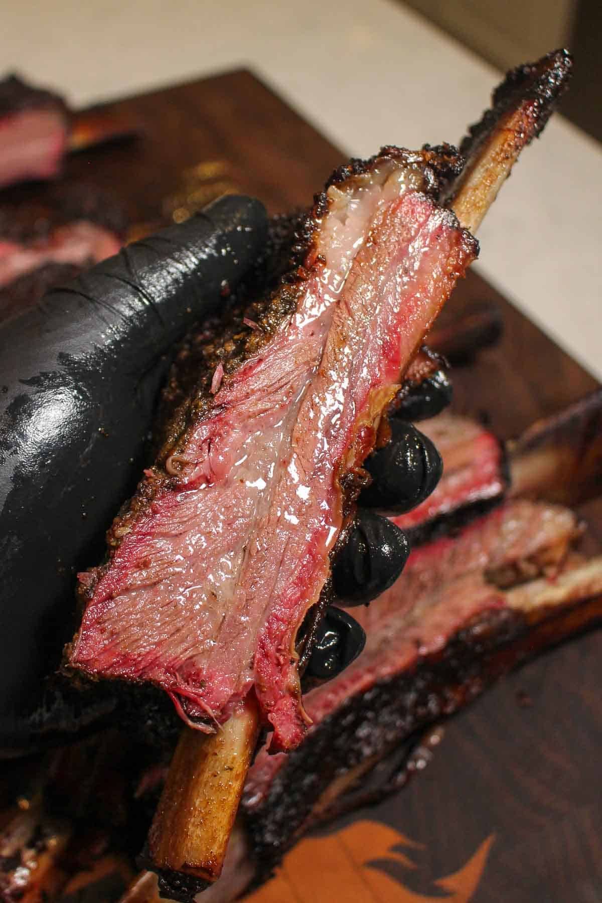 A single, sliced beef rib being held up to the camera so you can see the juiciness.