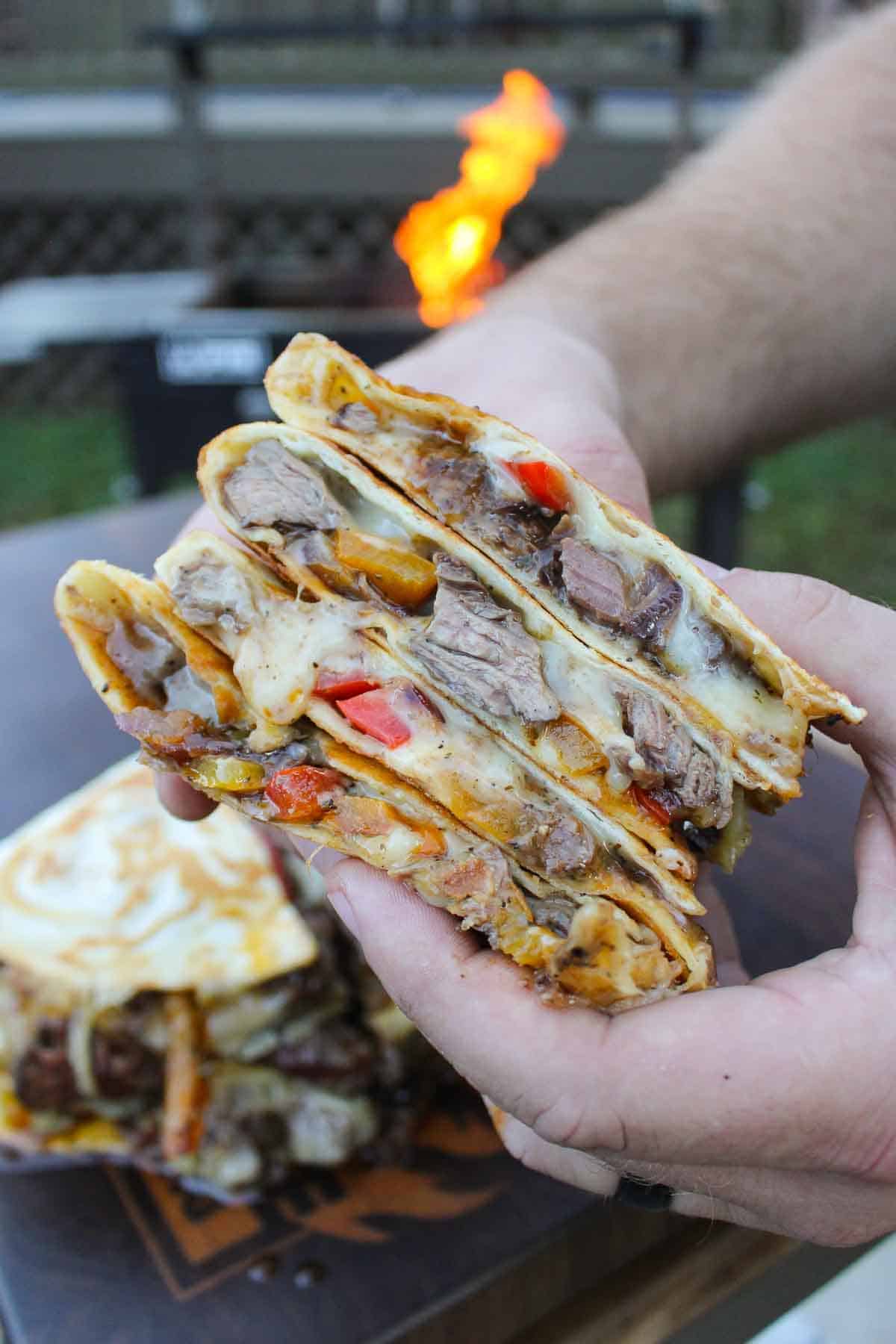 Hands holding a stack of sliced steak fajita quesadillas with cheese, peppers and steak