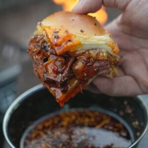 A close up of a hand holding a hot honey steak slider dipped in hot honey