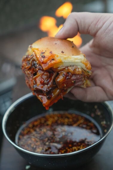 A close up of a hand holding a hot honey steak slider dipped in hot honey