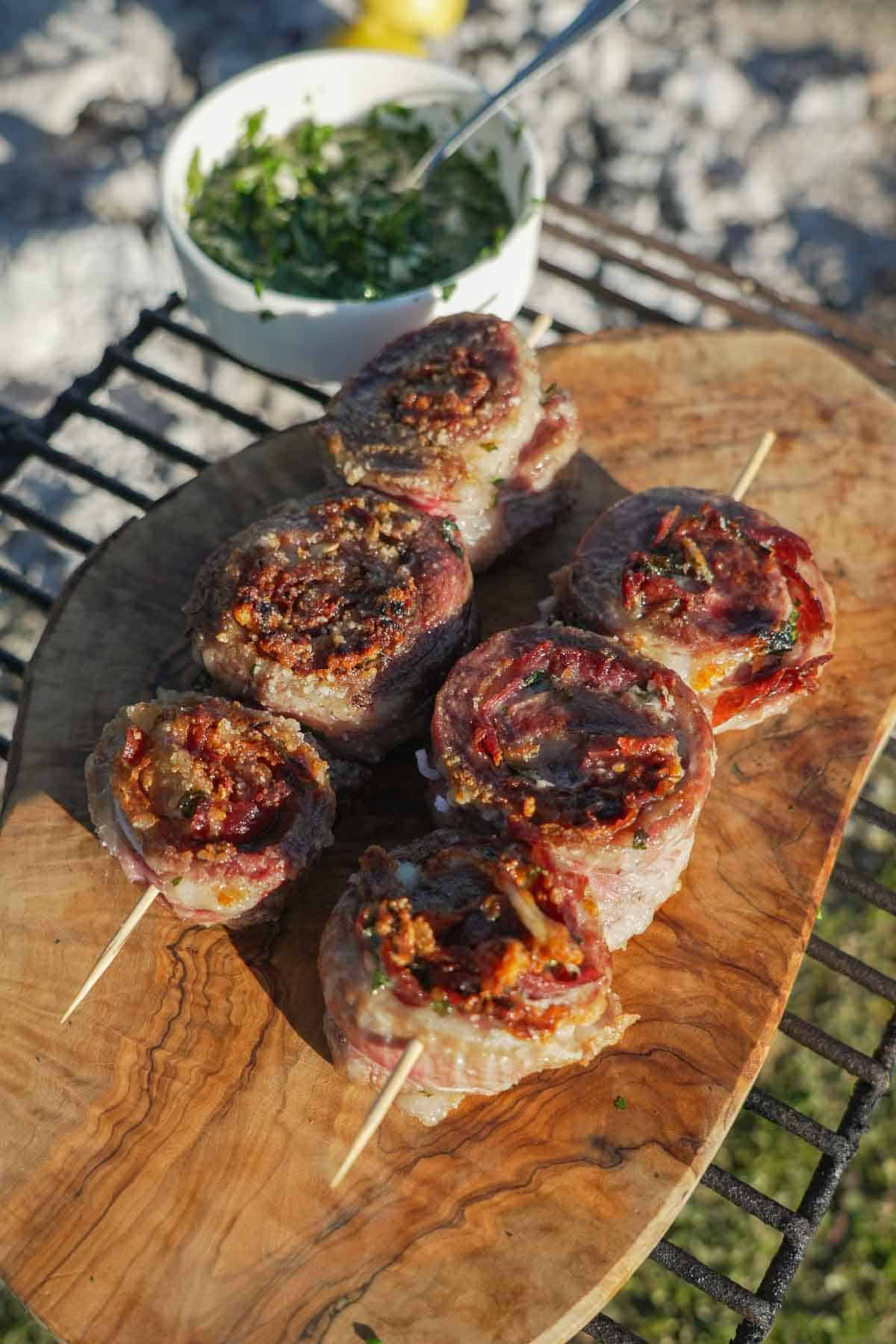 Cooked pork pinwheels with wooden skewers on a wooden cutting board with mojo verde sauce on the side