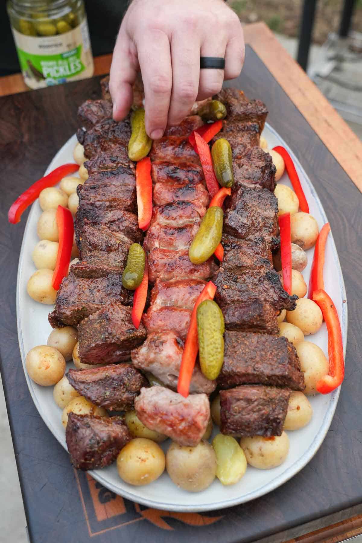 Assembling a platter of steak, sausages, raclette, potatoes, pickles and more