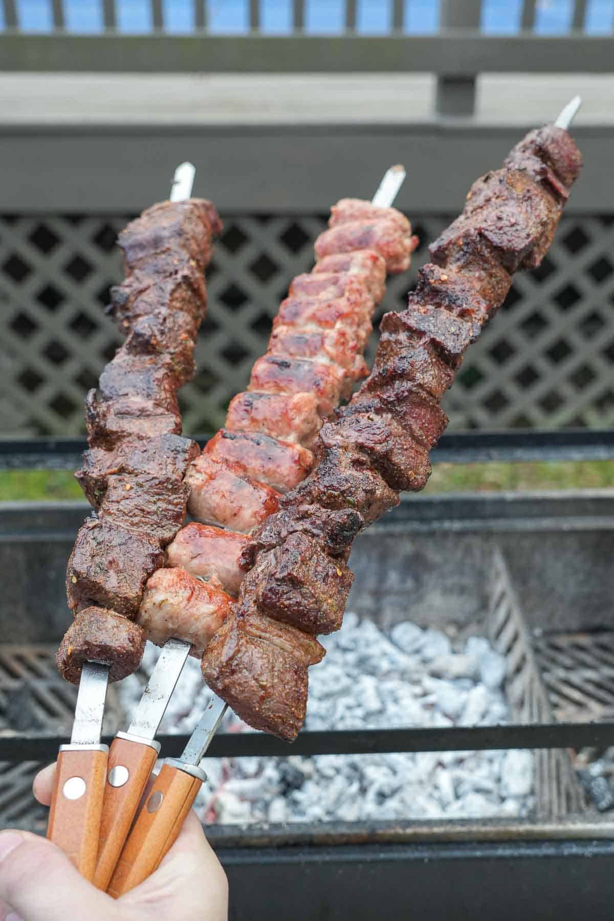 Pulling steak and sausage skewers off the grill to make grilled raclette