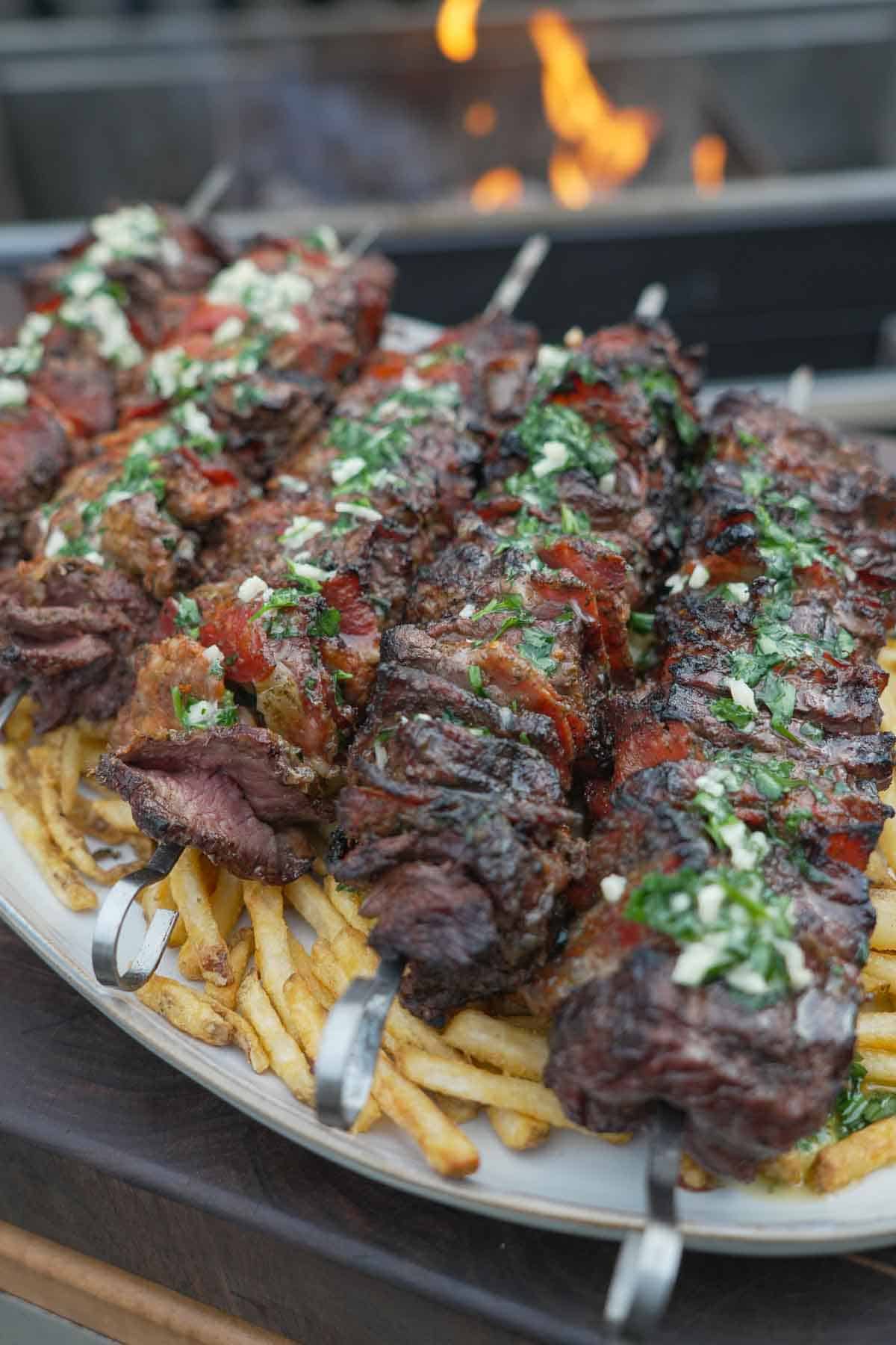 A close up of pizza steak skewers on a platter of French fries