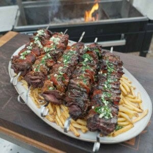 A plate of pizza steak skewers on top of fries and in front of a grill