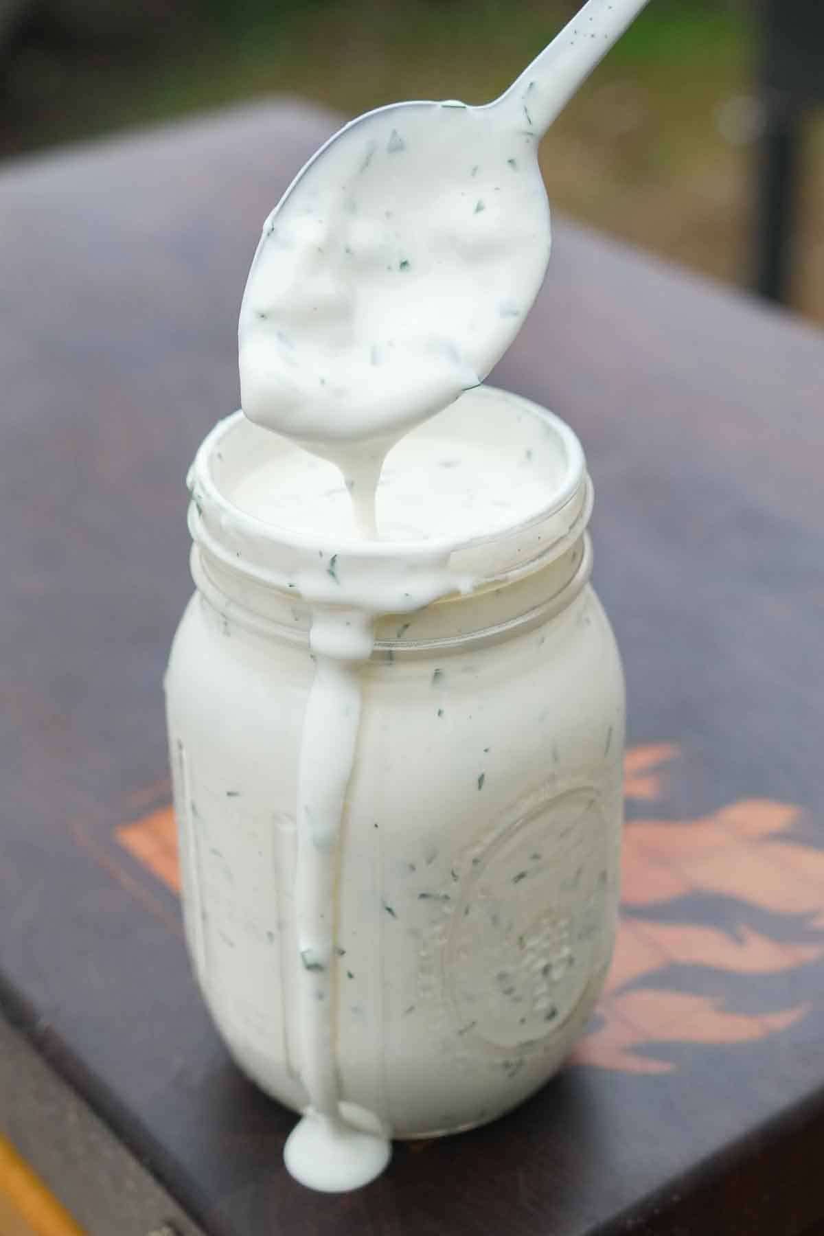 A mason jar filled with homemade ranch dressing and a spoon covered in dressing