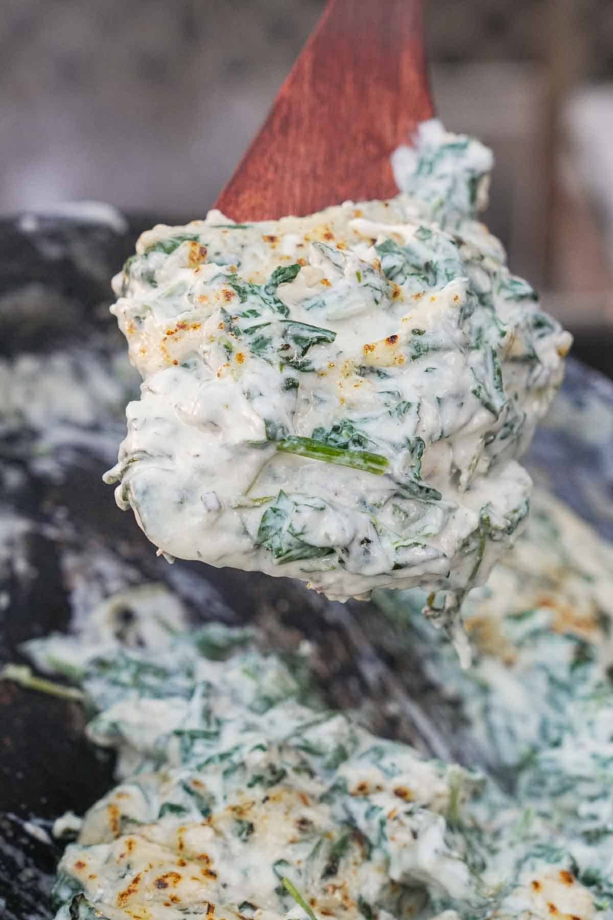 A spoonful of cream spinach above a cast iron skillet with the rest
