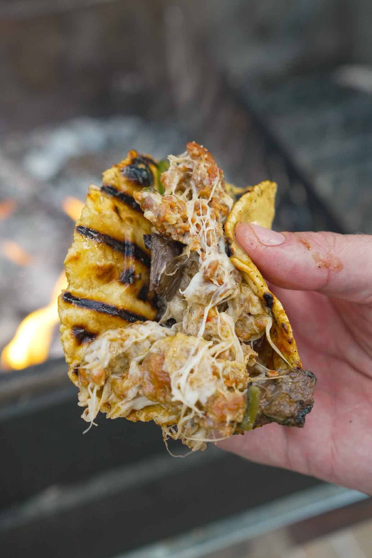A hand holding a tortilla stuffed full of queso flameado with chorizo and steak