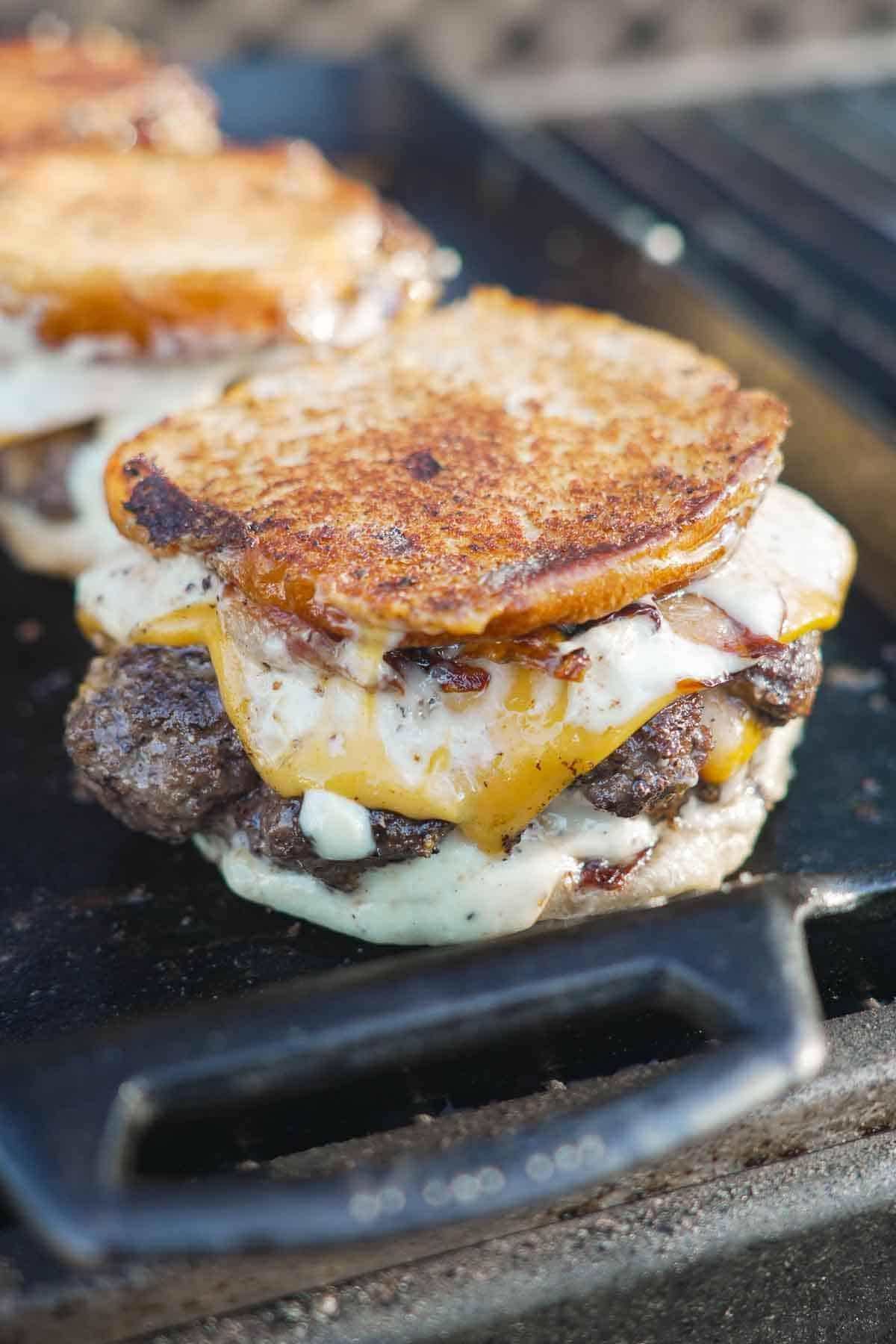 A fully assembled cheese stuffed patty melt with burger buns, bacon and garlic aioli
