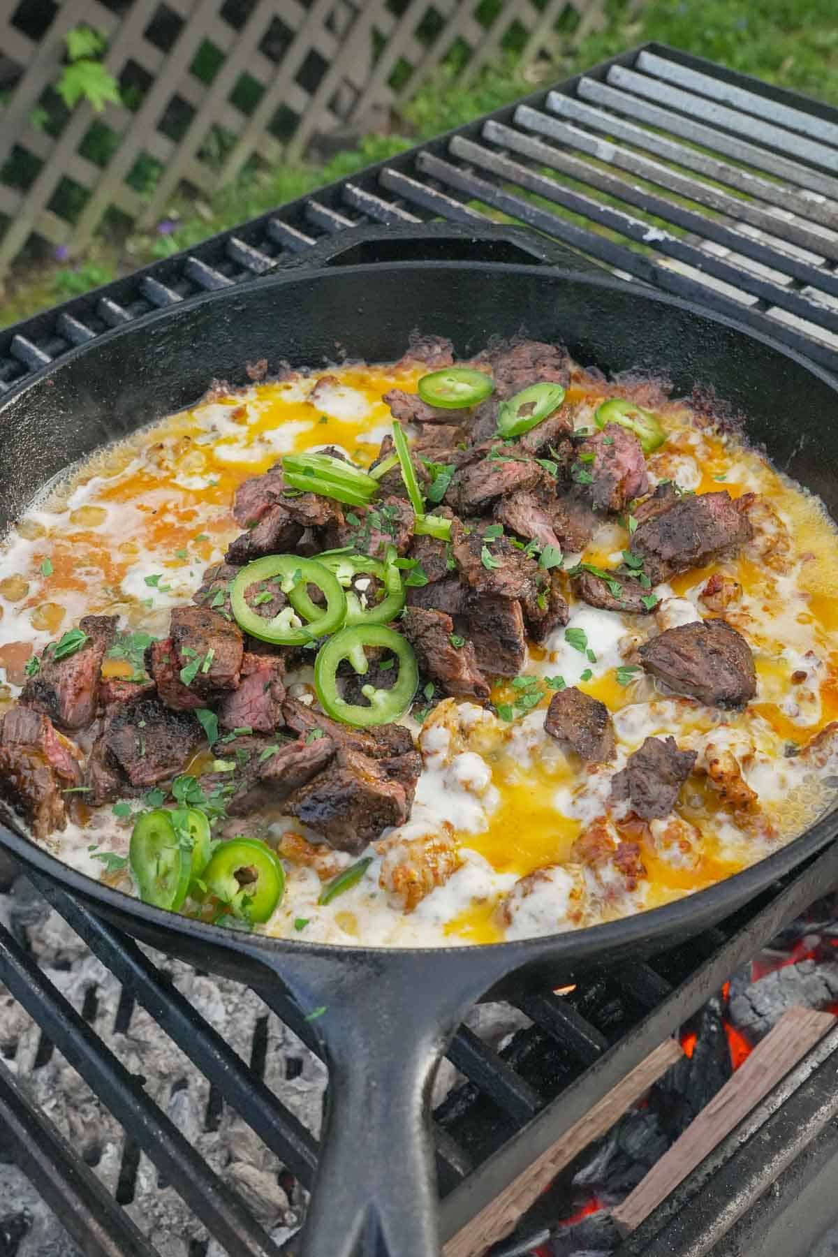 A cast iron skillet of queso flameado on the grill