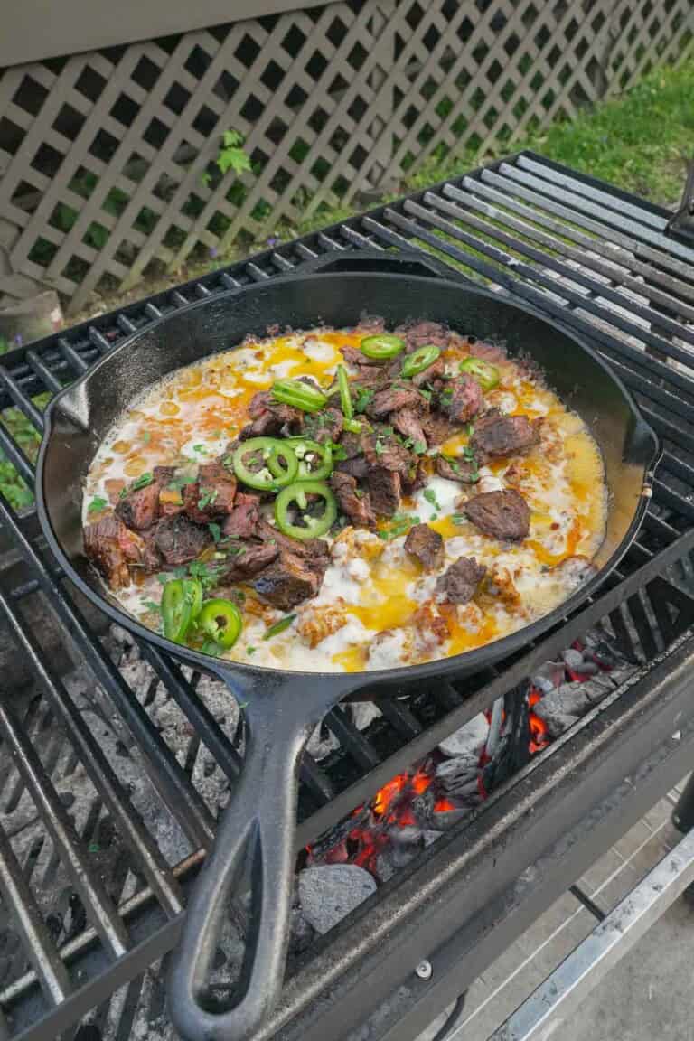 A cast iron skillet of queso flameado on the grill, with chopped cilantro and jalapeño slices for the garnish