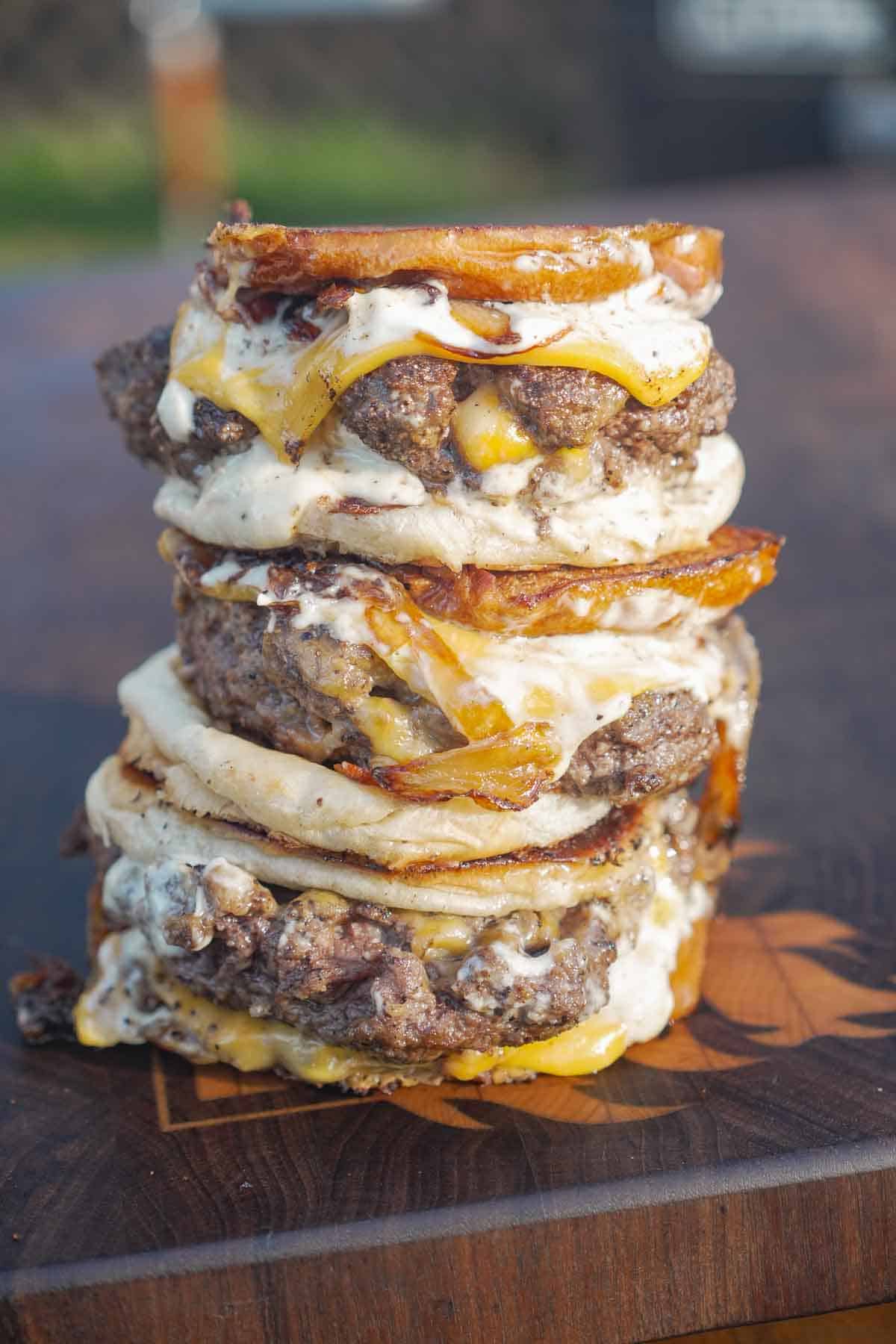 A stack of stuffed patty melts with burger buns, meat patties, bacon and garlic aioli