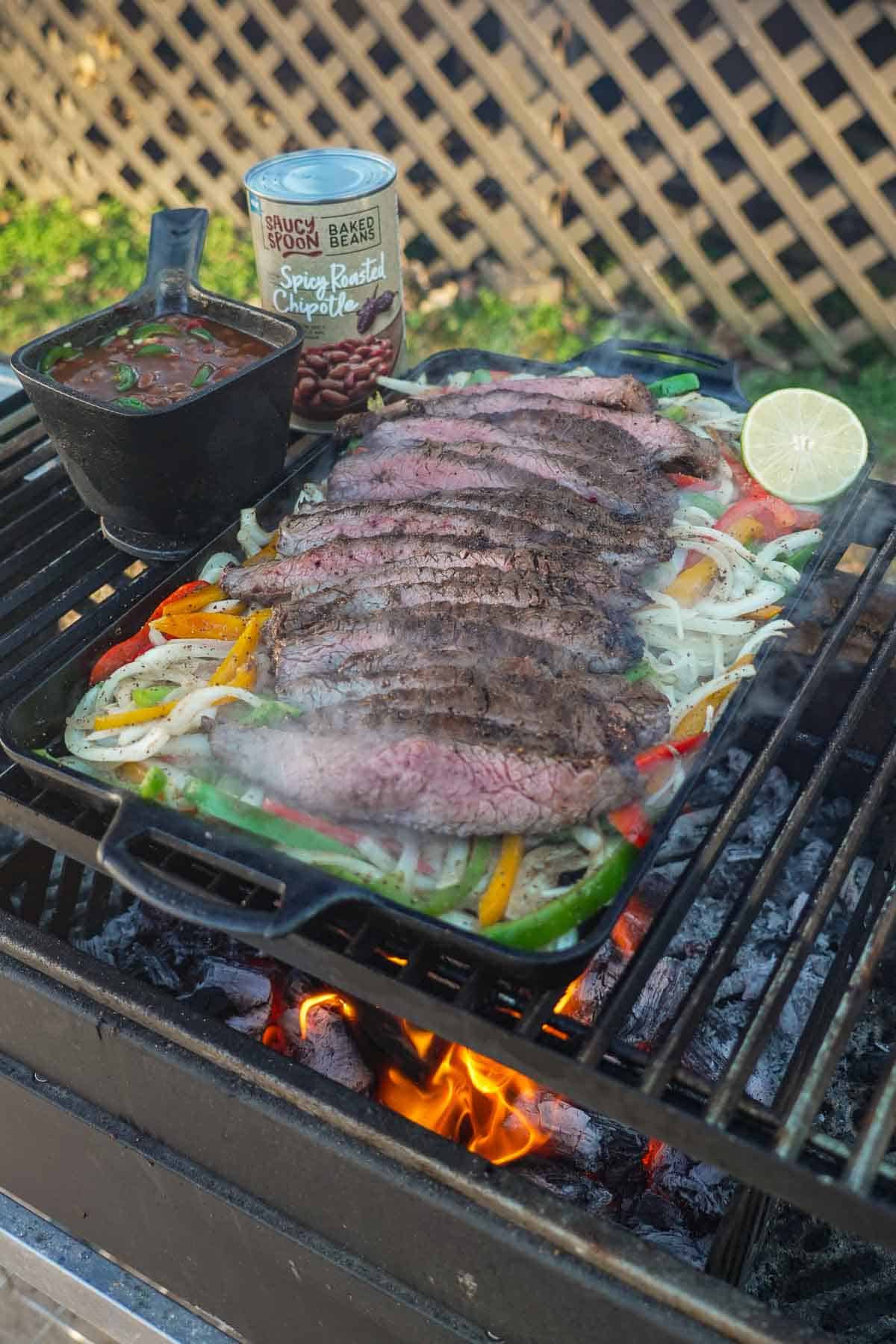 A plate of steak fajitas on the grill with Saucy Spoon baked beans and sliced limes